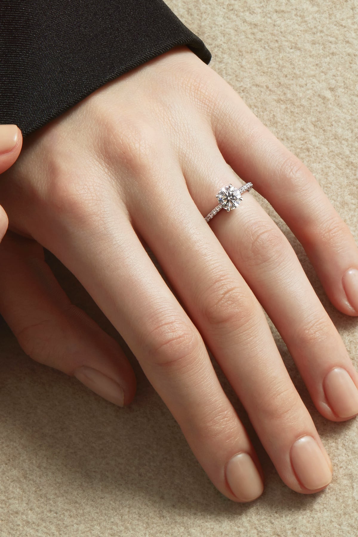 Close-up of a hand wearing a Hearts On Fire diamond ring on a beige background