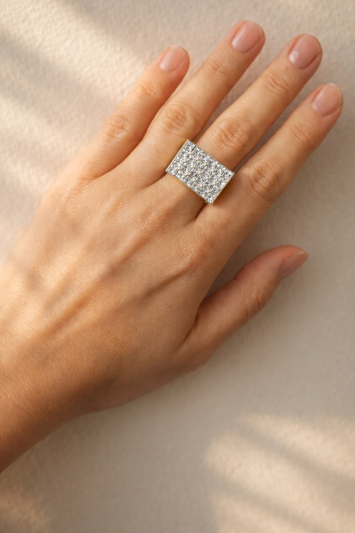 Hand wearing a diamond ring on a neutral background