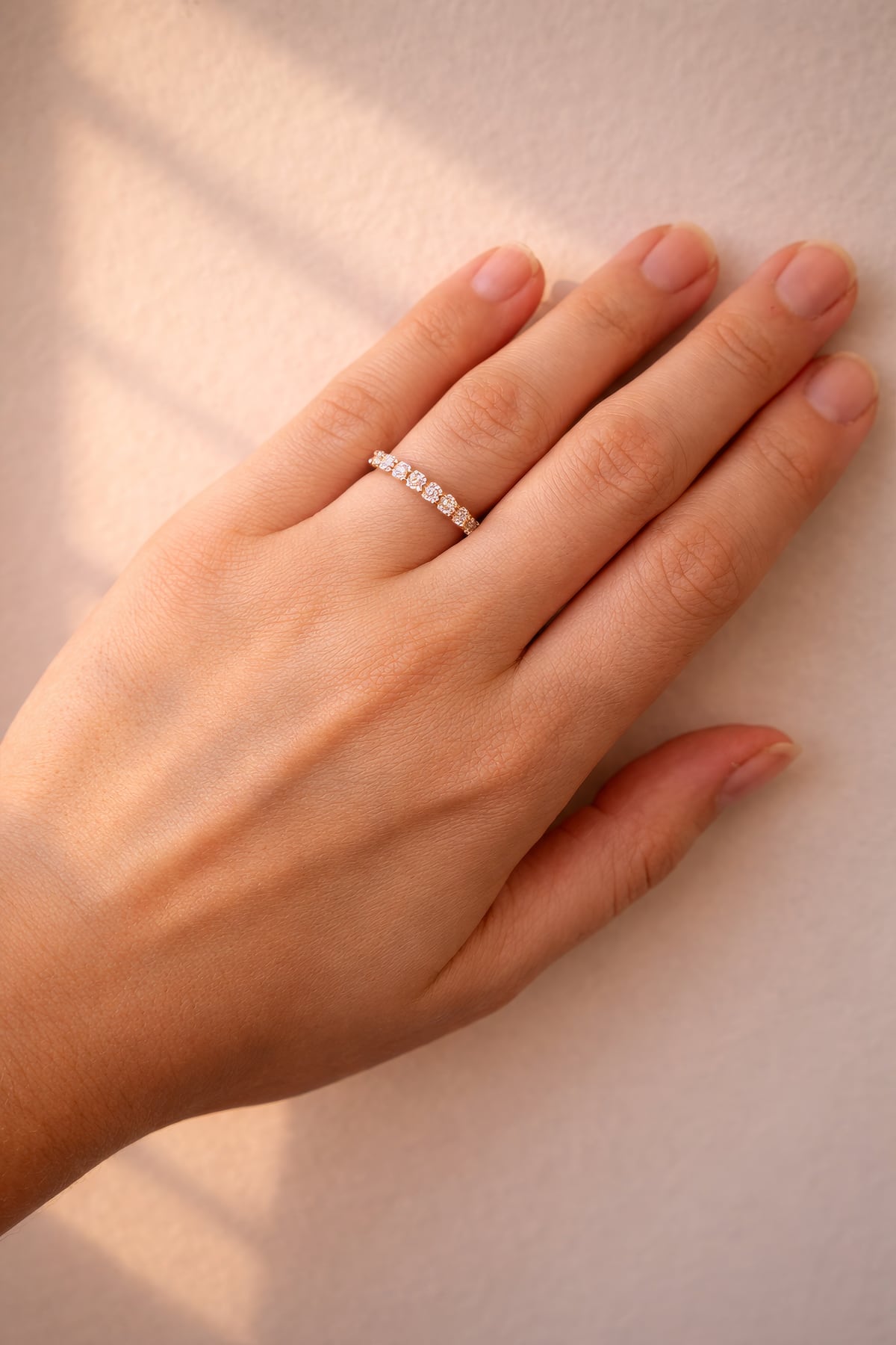 Hand wearing a rose gold diamond ring on a neutral background