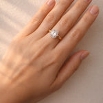 Hand wearing a gold ring with a diamond on a neutral background at LeGassick.