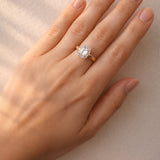 Hand wearing a gold ring with a diamond on a neutral background at LeGassick.
