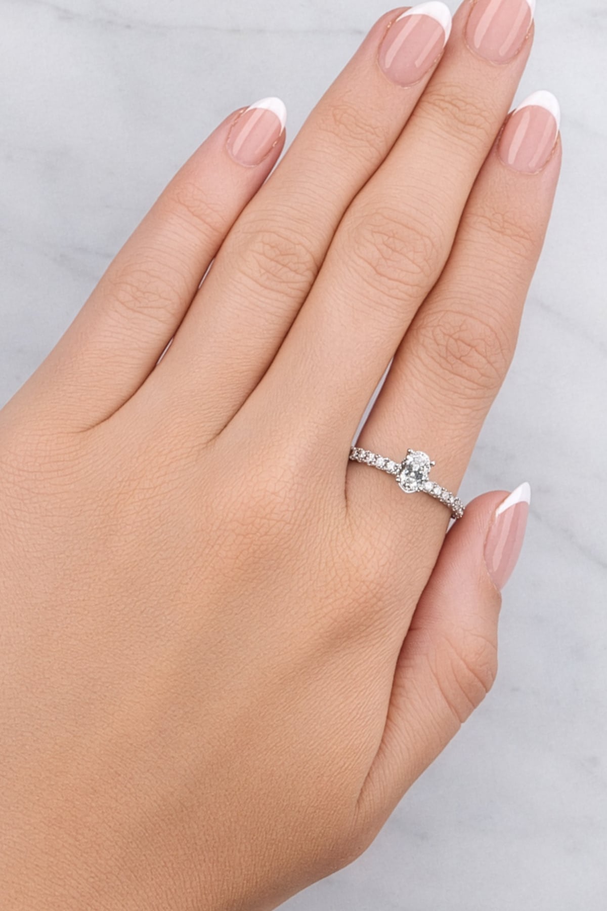 Hand wearing a silver ring with a diamond on a light grey background at LeGassick.