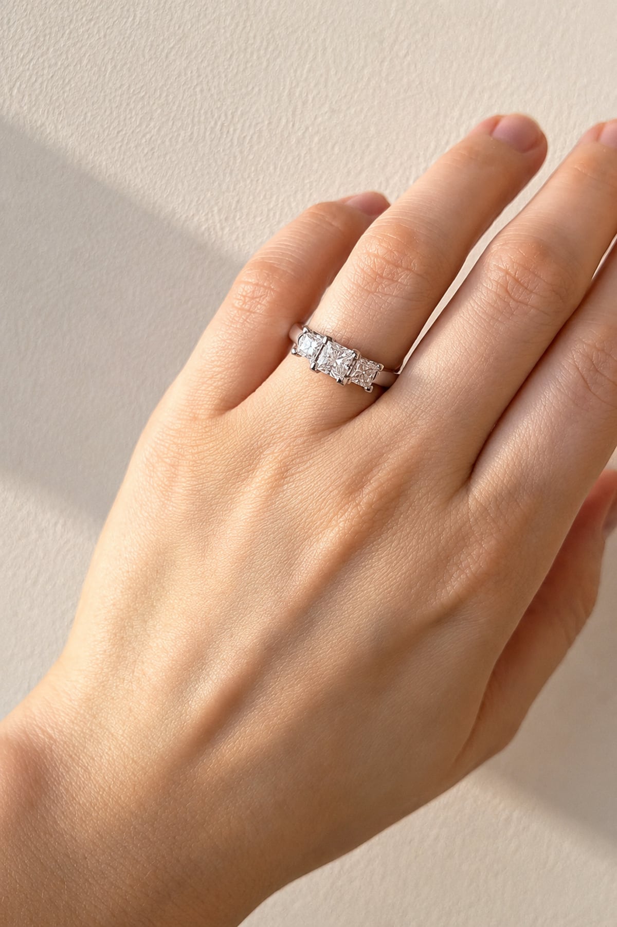 Hand wearing a Princess Cut Diamond Trilogy Ring in 18ct White Gold on a beige background