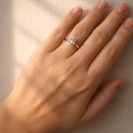 Hand wearing a gold ring with a diamond on a neutral background