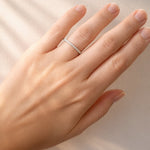 Hand wearing a white gold diamond band on a neutral background