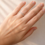 Hand wearing a white gold diamond band on a neutral background