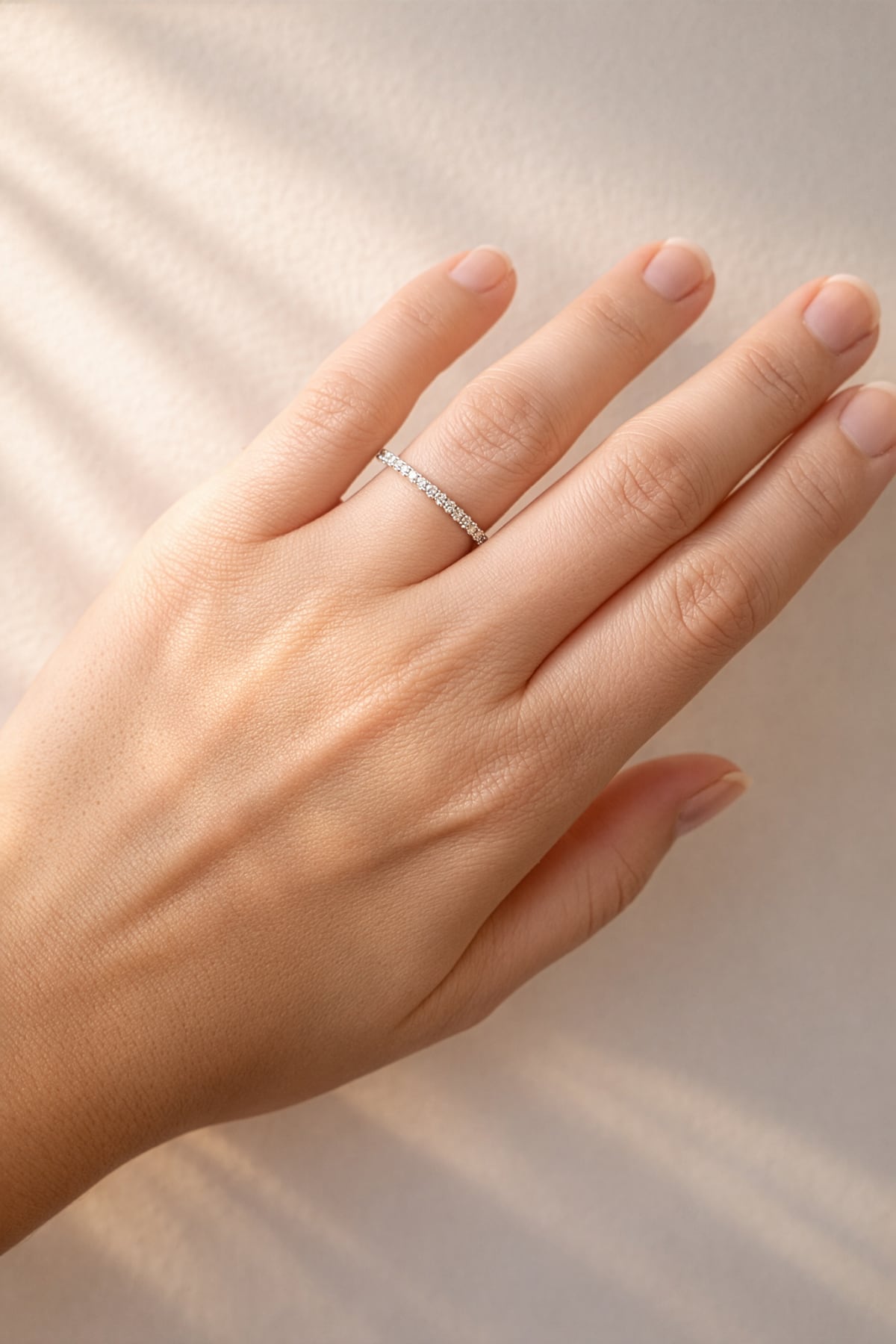 Hand wearing a white gold diamond band on a neutral background