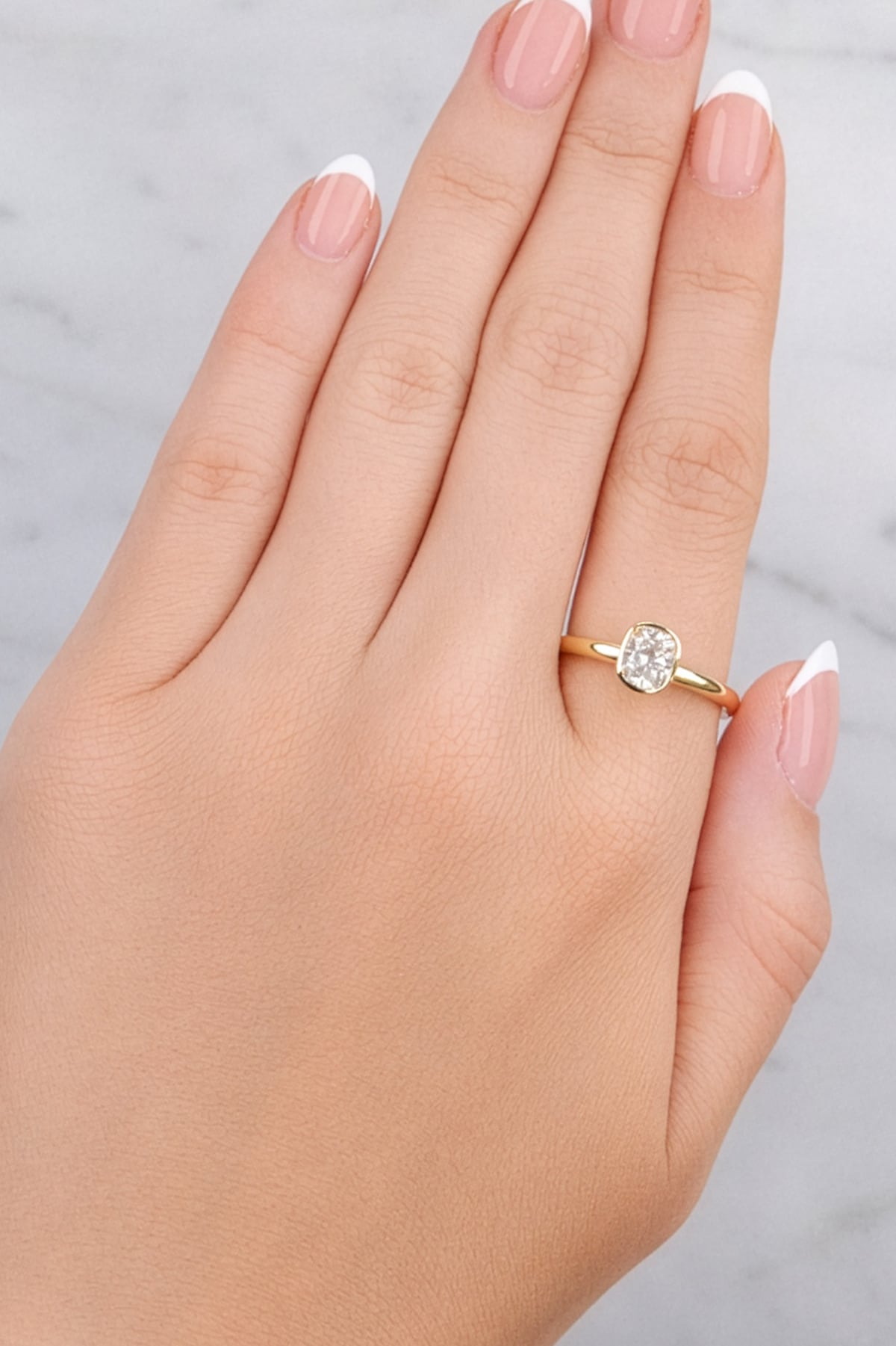 Hand wearing a gold ring with a diamond on a light gray background at LeGassick.