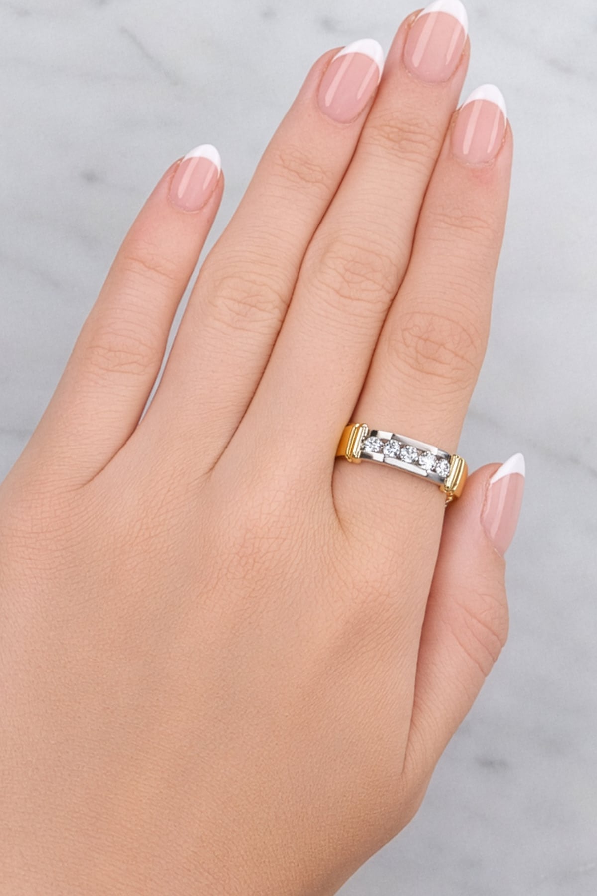 Hand wearing a gold and silver ring on a neutral background at LeGassick.