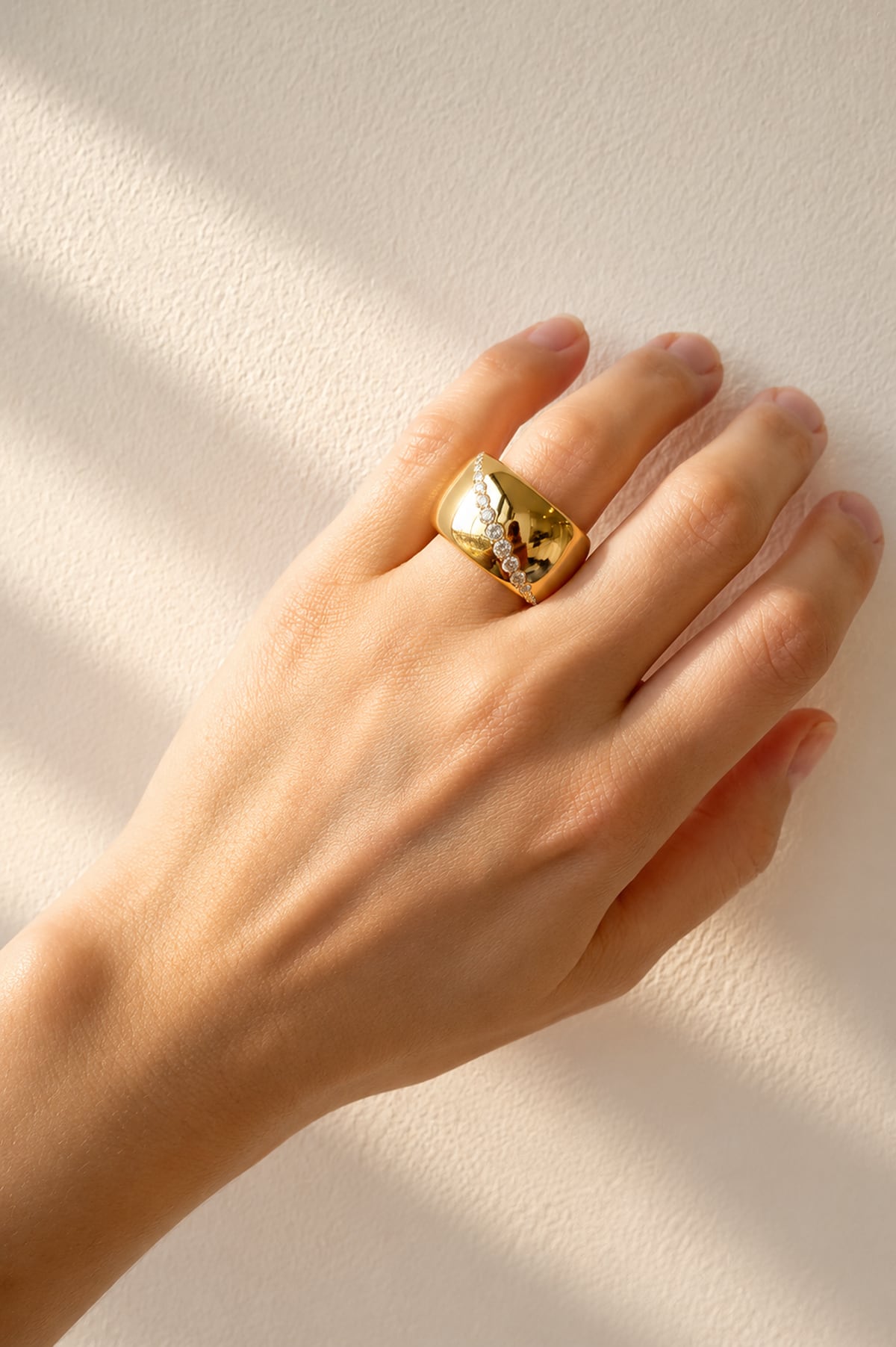 Hand wearing an Italian gold ring with a stone on a beige background