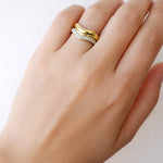 Hand wearing a gold ring with a white gemstone on a light background