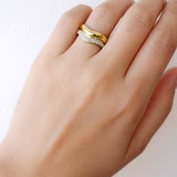 Hand wearing a gold ring with a white gemstone on a light background
