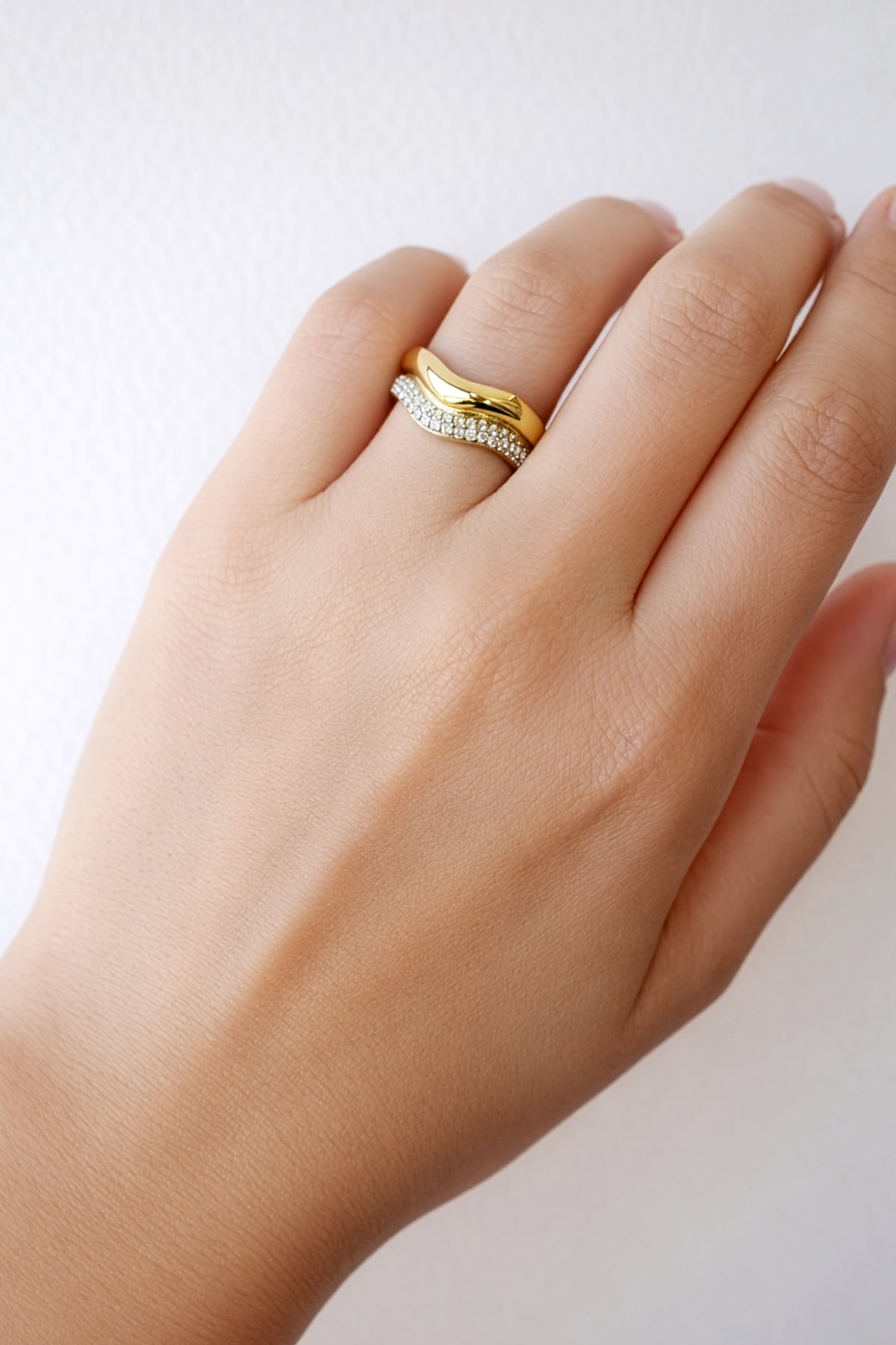 Hand wearing a gold ring with a white gemstone on a light background