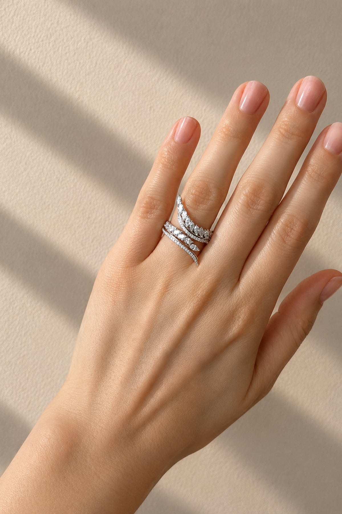 A close-up of a hand wearing a delicate white gold ring set with small clear diamonds, photographed against a warm beige background with soft diagonal shadows.