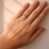 Hand wearing a gold ring with emeralds and diamonds on a white background