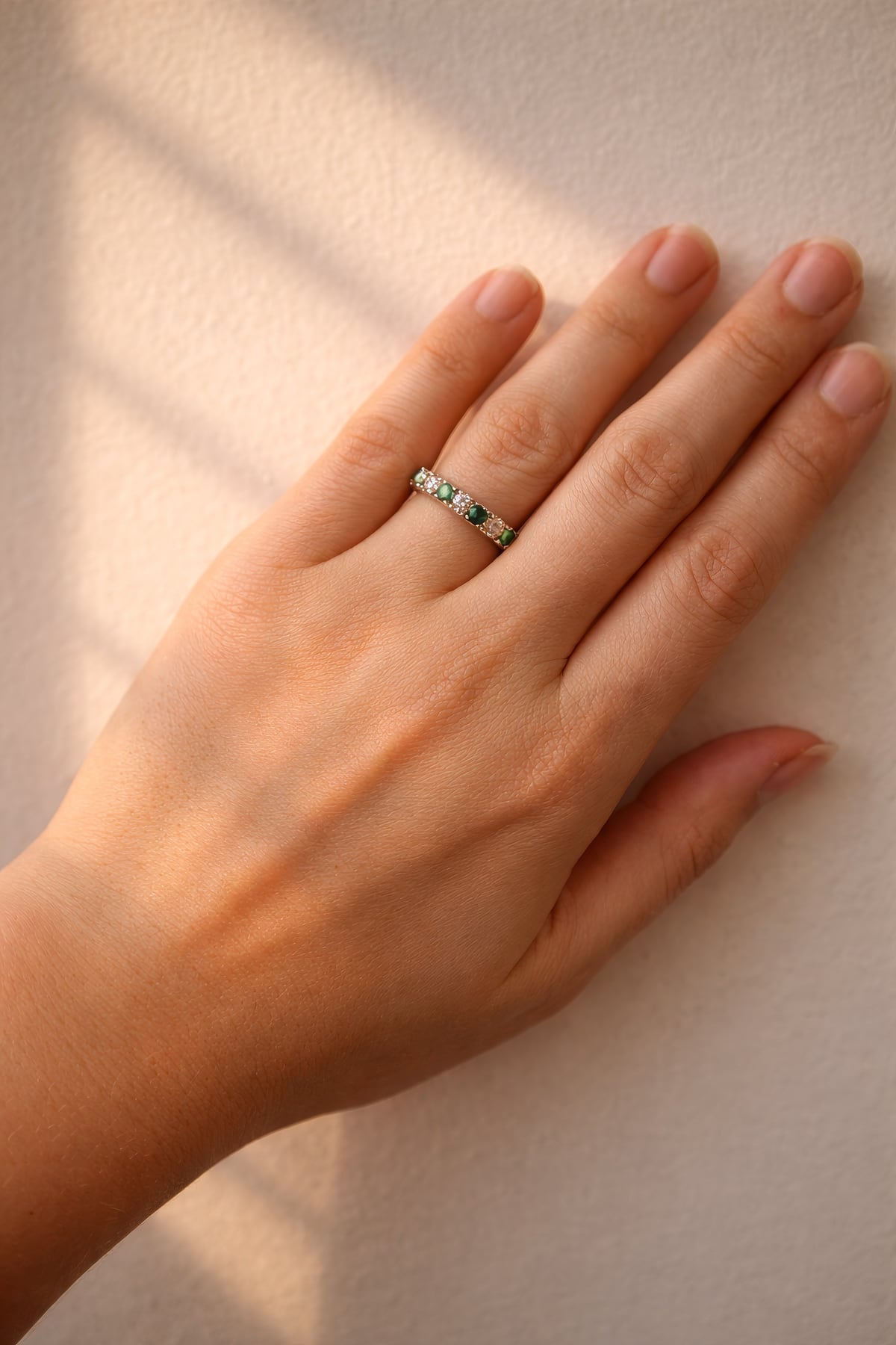 Hand wearing a gold ring with emeralds and diamonds on a white background