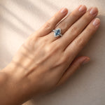 Hand wearing a ring with a blue gemstone on a neutral background at LeGassick.