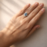Hand wearing a ring with a blue gemstone on a neutral background at LeGassick.