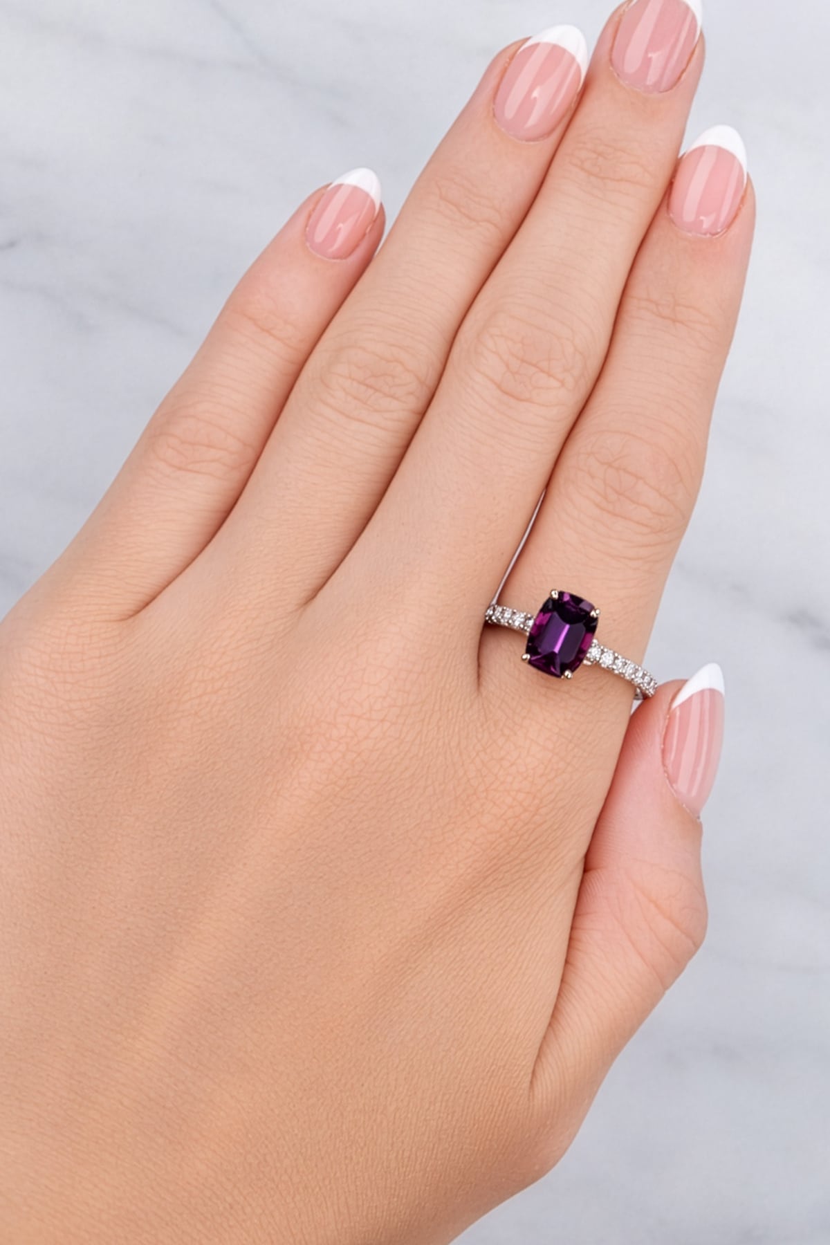 Hand wearing a ring with a purple gemstone on a light background at LeGassick Showroom.