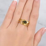 Gold ring with a green gemstone on a hand against a light background