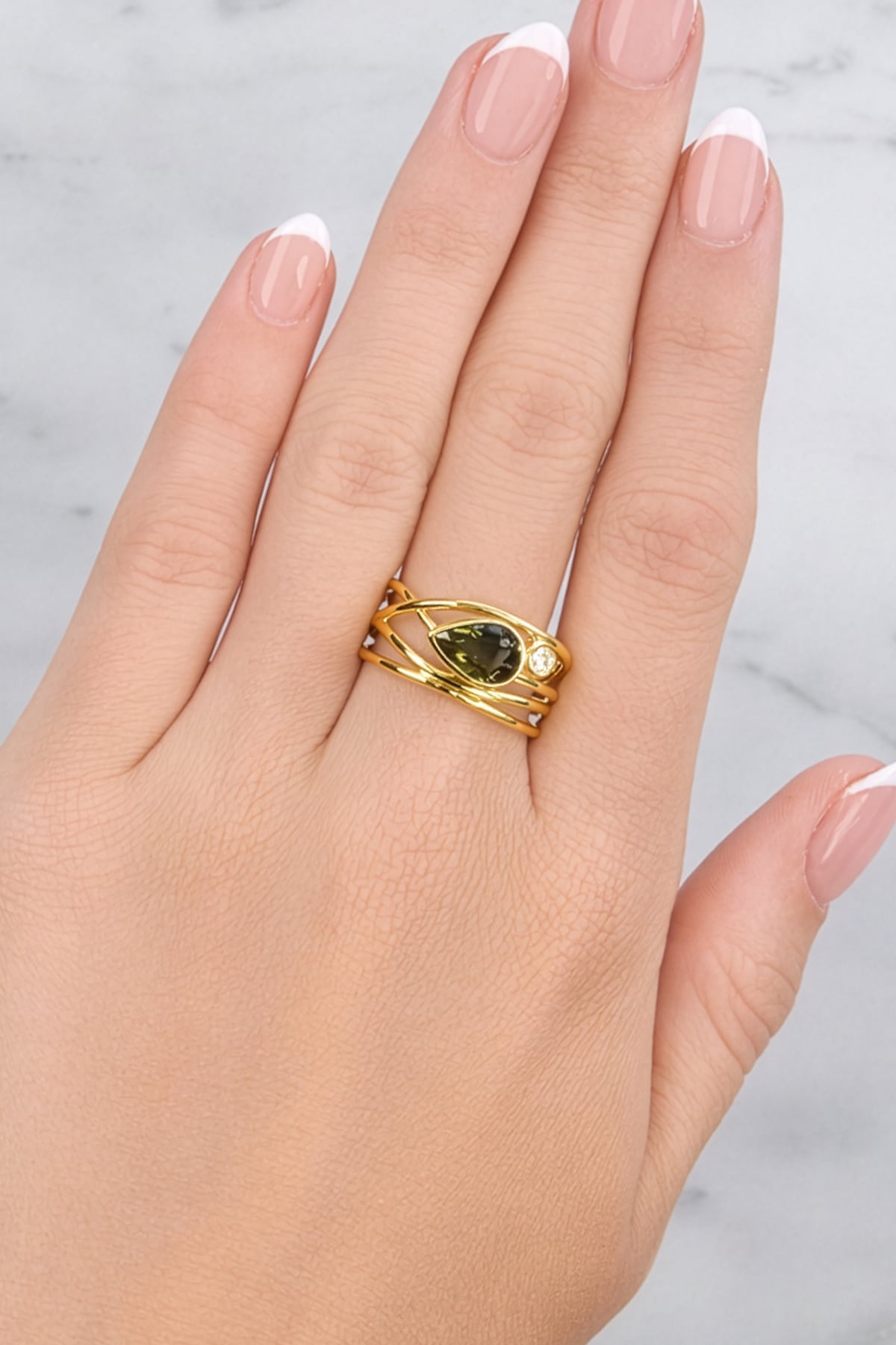 Gold ring with a green gemstone on a hand against a light background