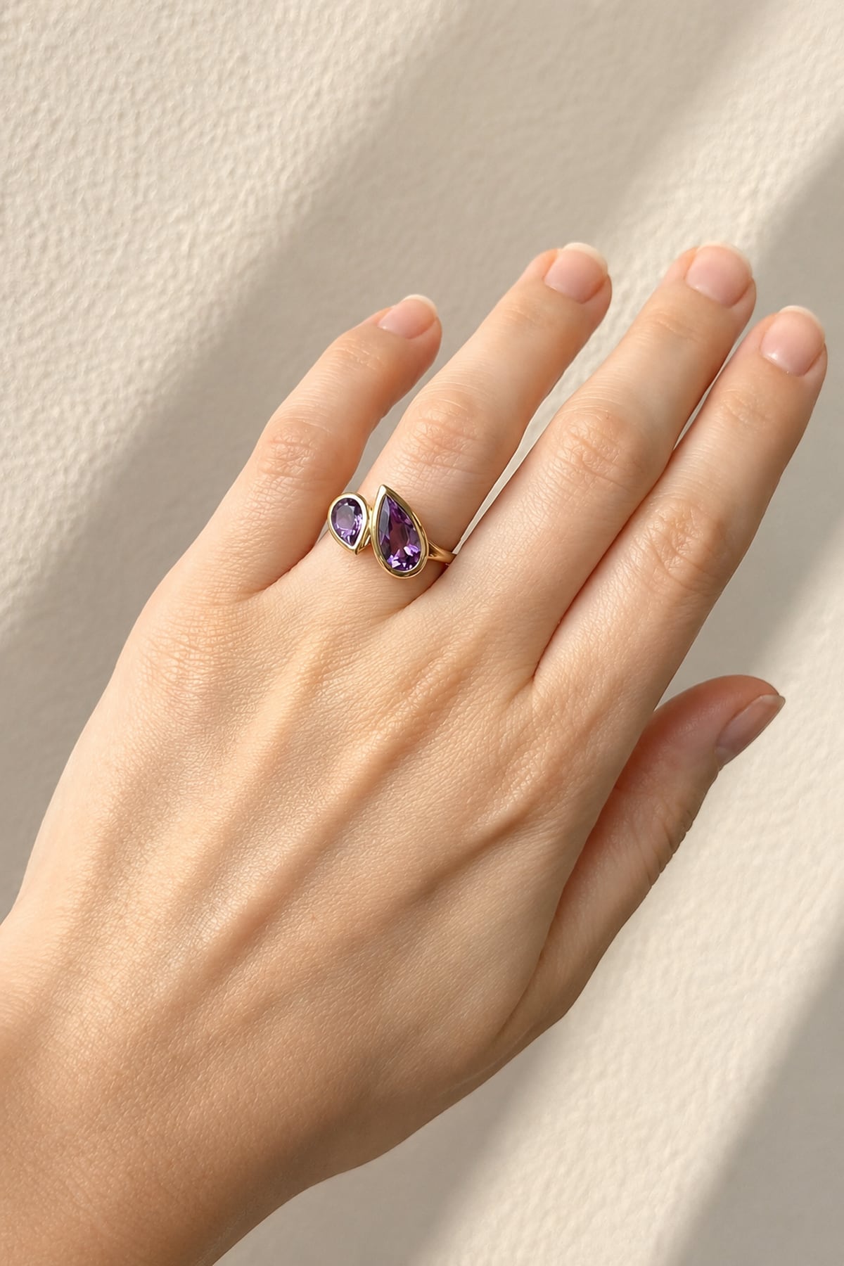 Hand wearing a Amethyst Toi et Moi Yellow Gold Ring on beige background