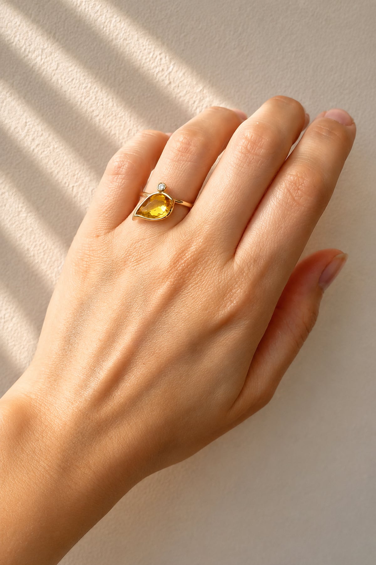 Hand wearing a Citrine & Diamond Leaf Motif Ring in Yellow Gold on a beige background