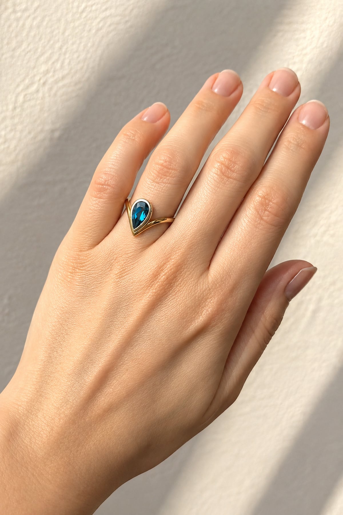 Hand wearing a London Blue Topaz Ring in Yellow & White Gold on a beige background