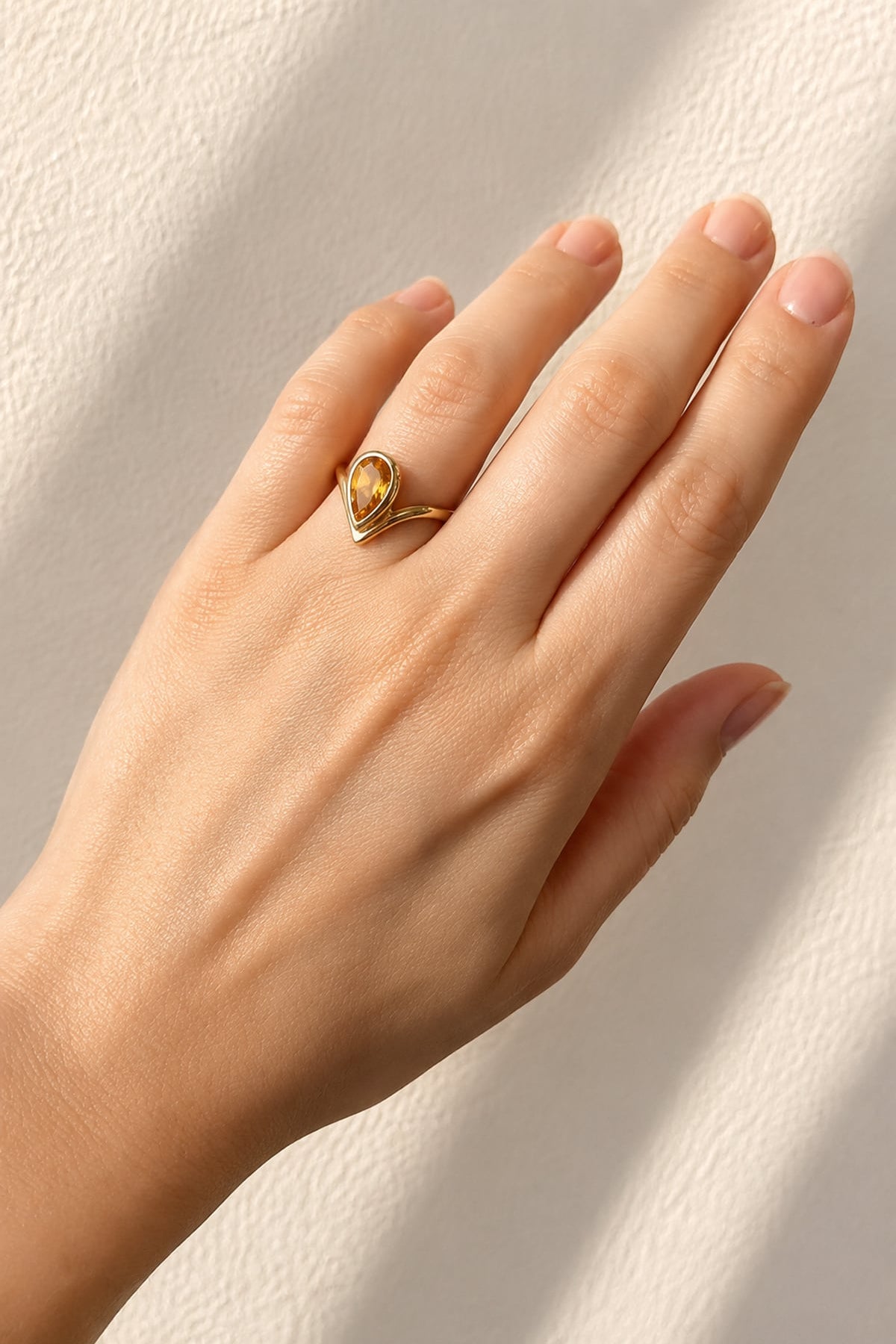Hand wearing a Pear Cut Bezel Set Citrine Ring in Yellow Gold on a light background