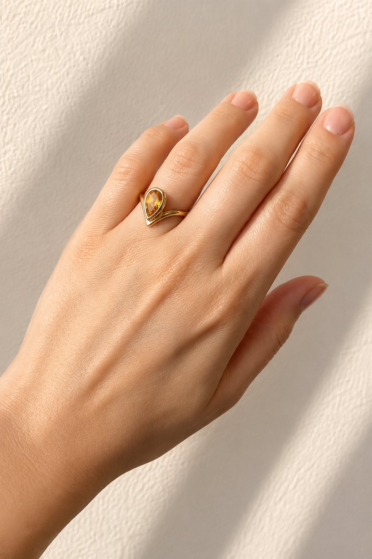Hand wearing a Pear Cut Bezel Set Citrine Ring in Yellow Gold on a light background