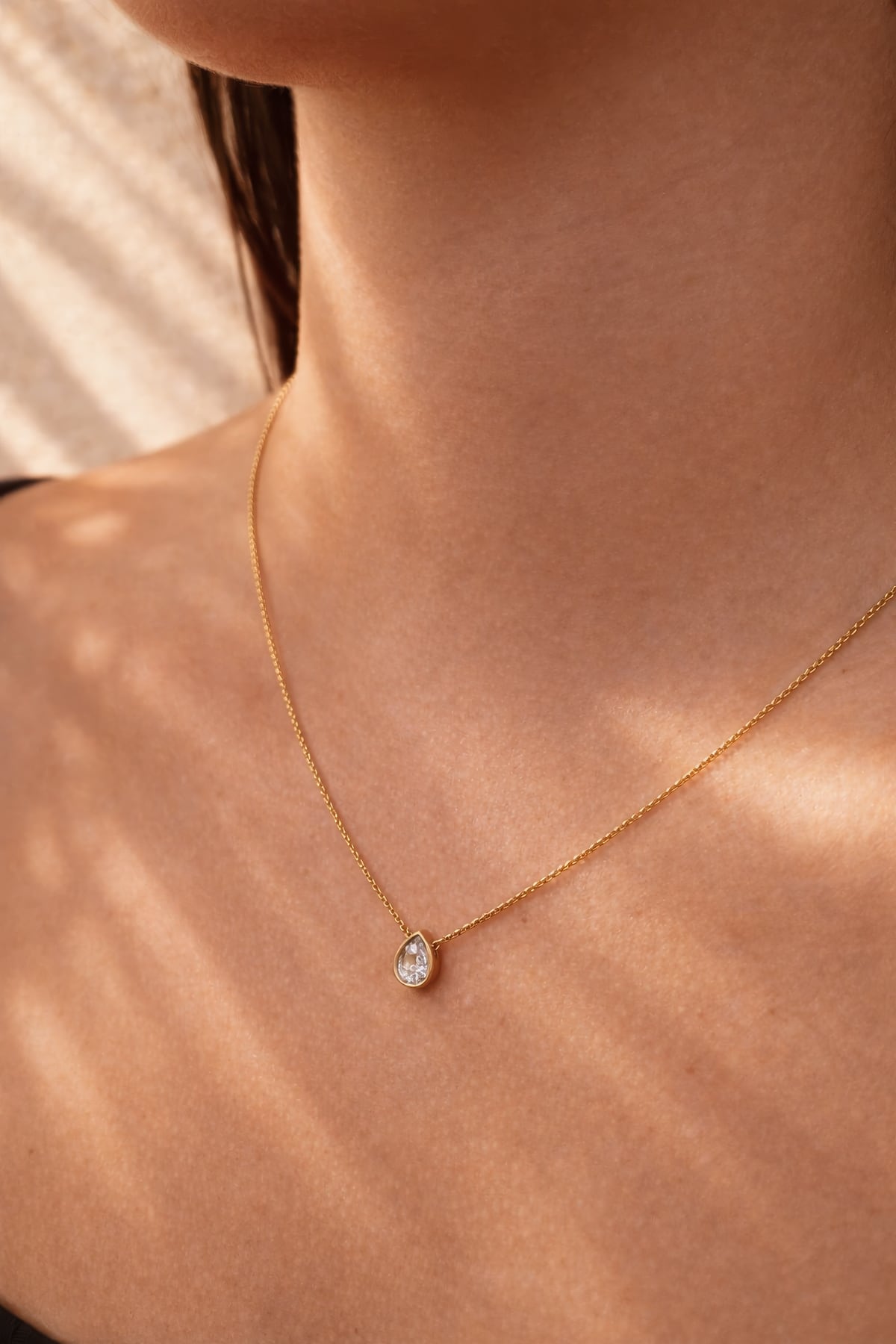 Gold necklace with a diamond teardrop pendant on a person's neck at LeGassick