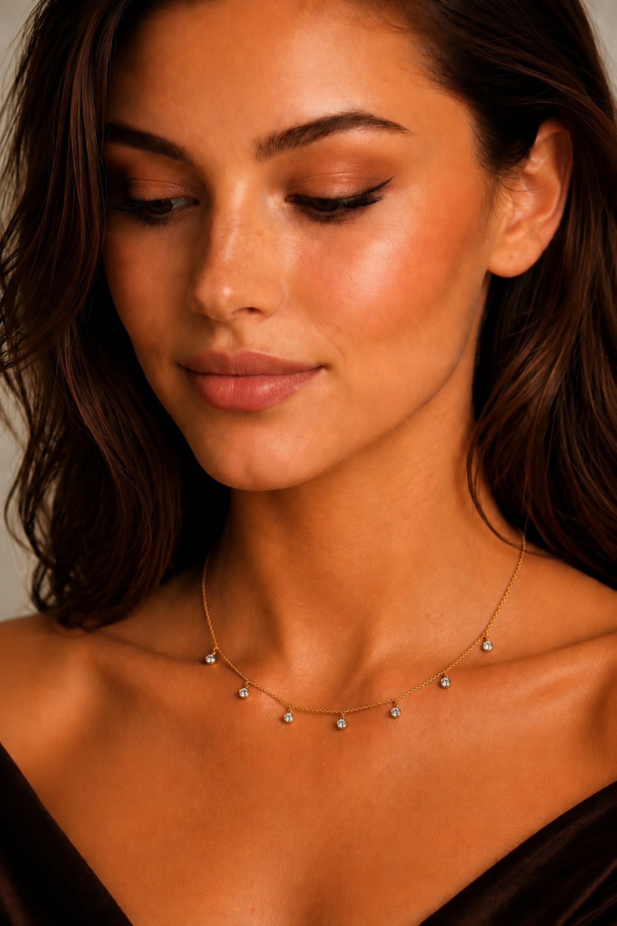 A close-up of a woman wearing a delicate gold chain necklace with small, clear, round-cut diamonds spaced along the chain.