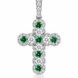 A white gold cross pendant featuring a central cluster of round green emeralds surrounded by pavé-set clear diamonds, shown on a white background with a soft reflection.
