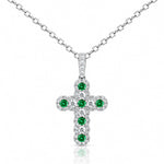 A white gold cross pendant featuring a central cluster of round green emeralds surrounded by pavé-set clear diamonds, shown on a white background with a soft reflection.