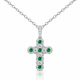 A white gold cross pendant featuring a central cluster of round green emeralds surrounded by pavé-set clear diamonds, shown on a white background with a soft reflection.