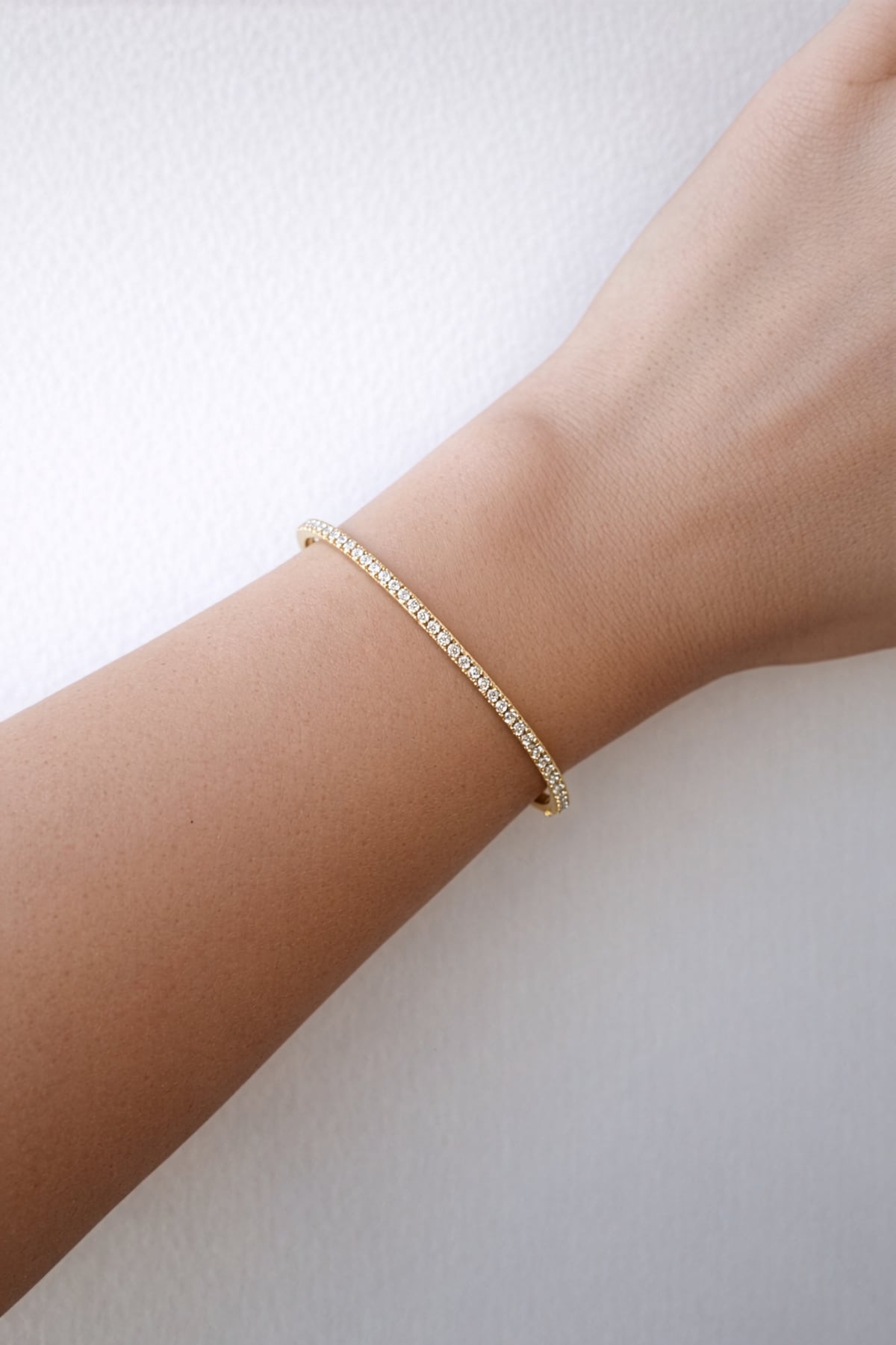 Gold diamond Bangle on a wrist against a light background