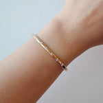 Gold bracelet on a wrist against a light gray background