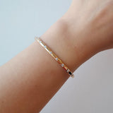 Gold bracelet on a wrist against a light gray background