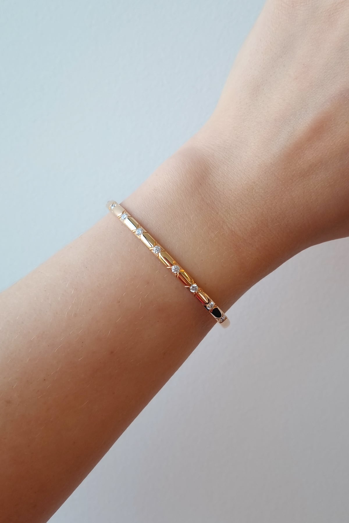 Gold bracelet on a wrist against a light gray background