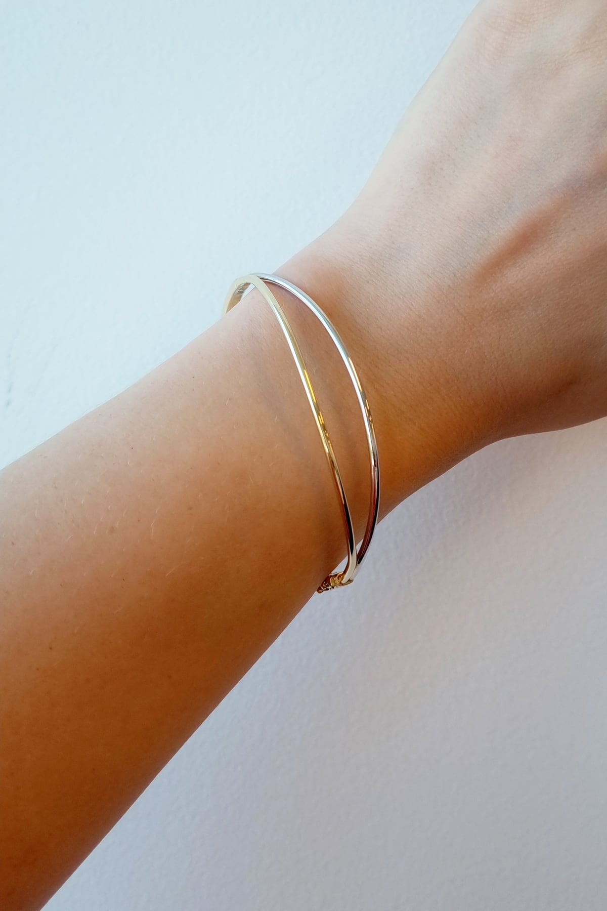 Gold bracelet on a wrist against a light background