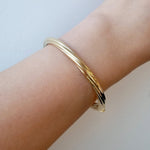 Gold bracelet on a wrist against a light background