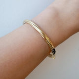 Gold bracelet on a wrist against a light background