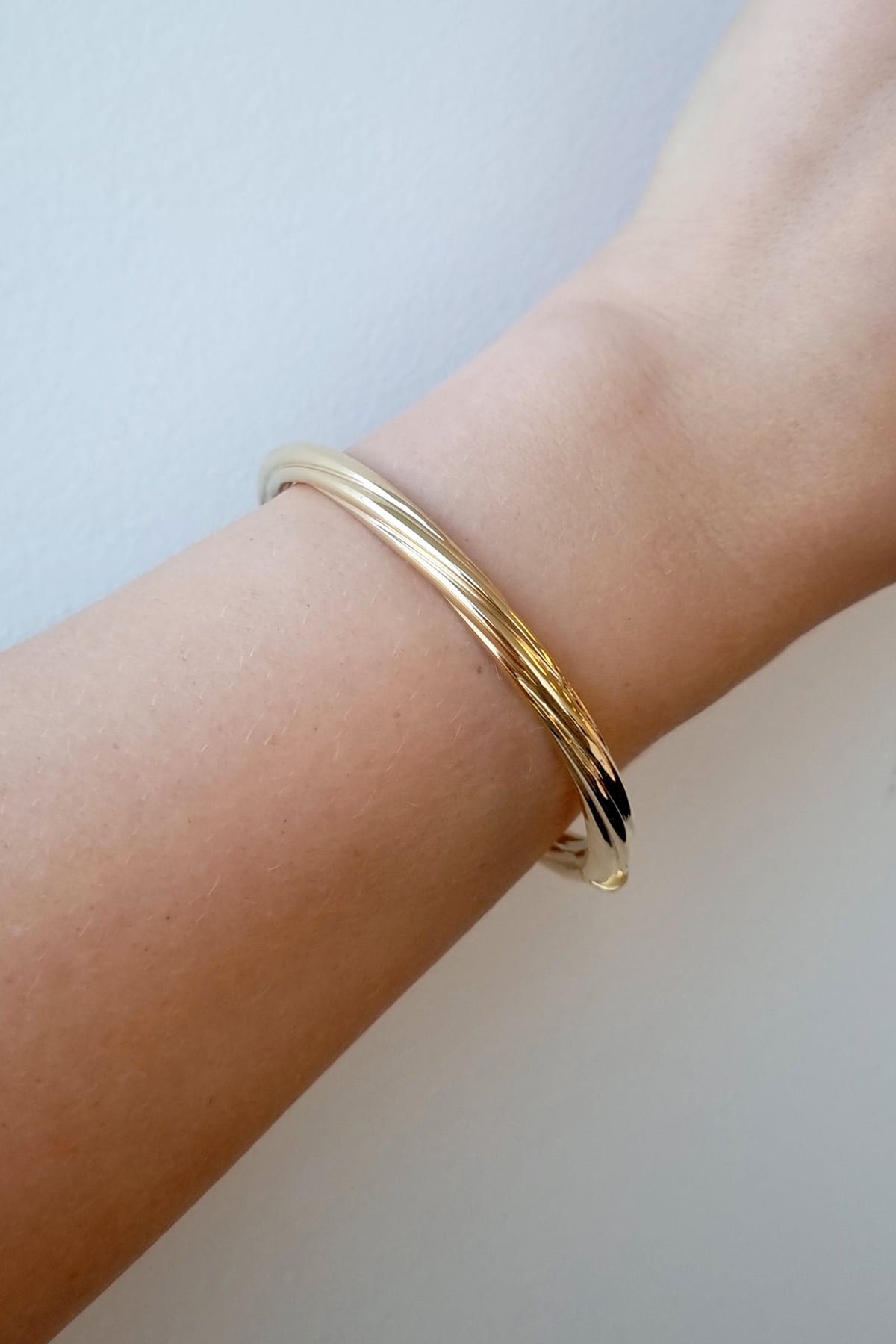 Gold bracelet on a wrist against a light background