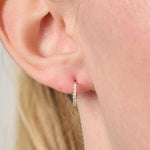 Close-up of an ear wearing a small hoop earring with a plain background