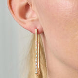 Gold hoop earring with clear stones worn by a person against a neutral background