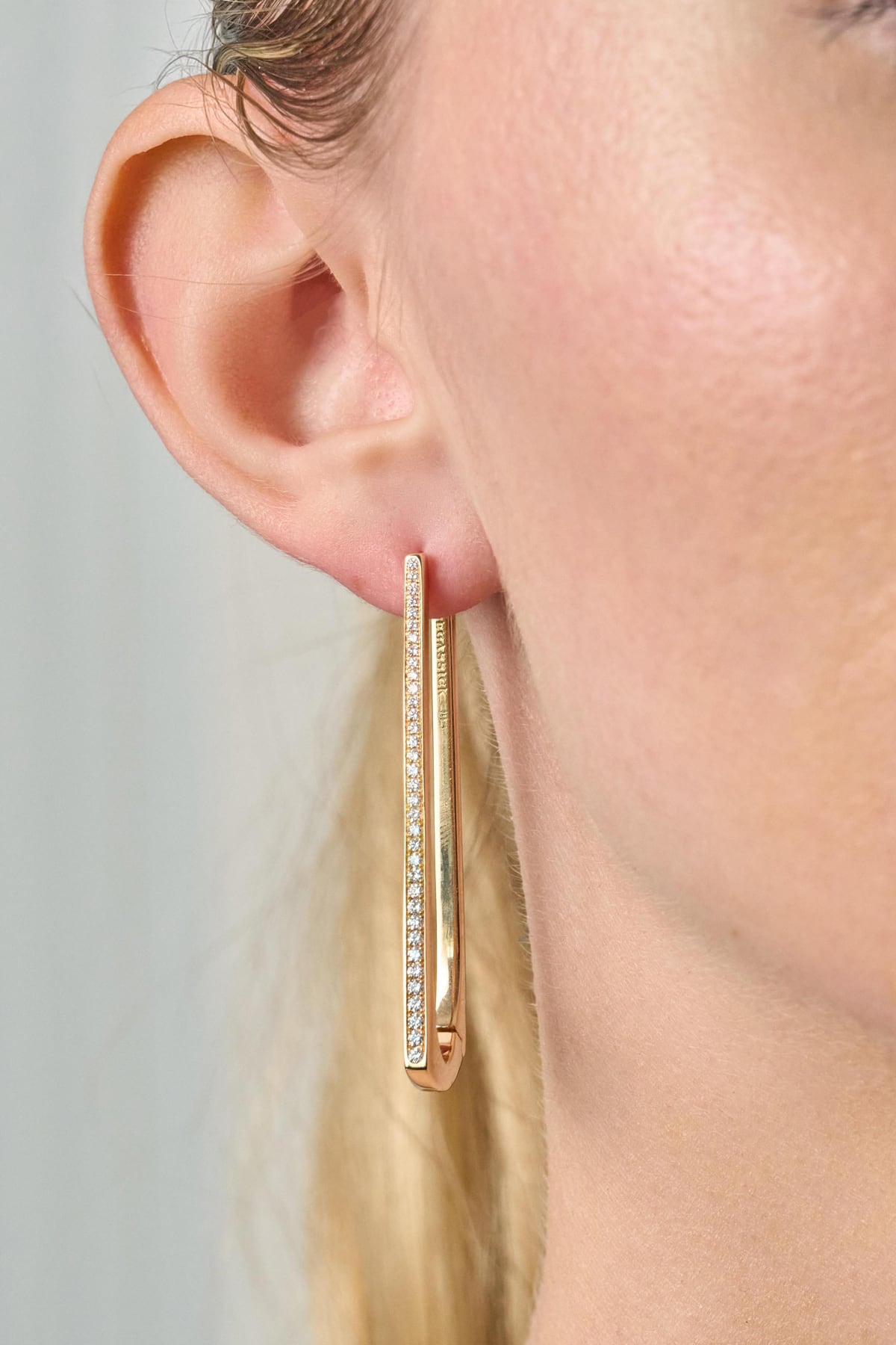 Gold hoop earring with clear stones worn by a person against a neutral background