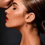 Lady wearing Amethyst & Diamond Drop Earrings in Yellow Gold on a grey background