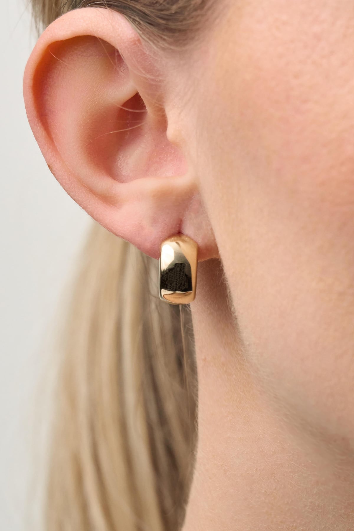Gold hoop earring worn by a person with a neutral background