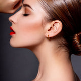Woman with styled hair, gold earrings and red lipstick against a dark background