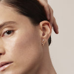 Close-up of a woman wearing a gold earring with a beige background
